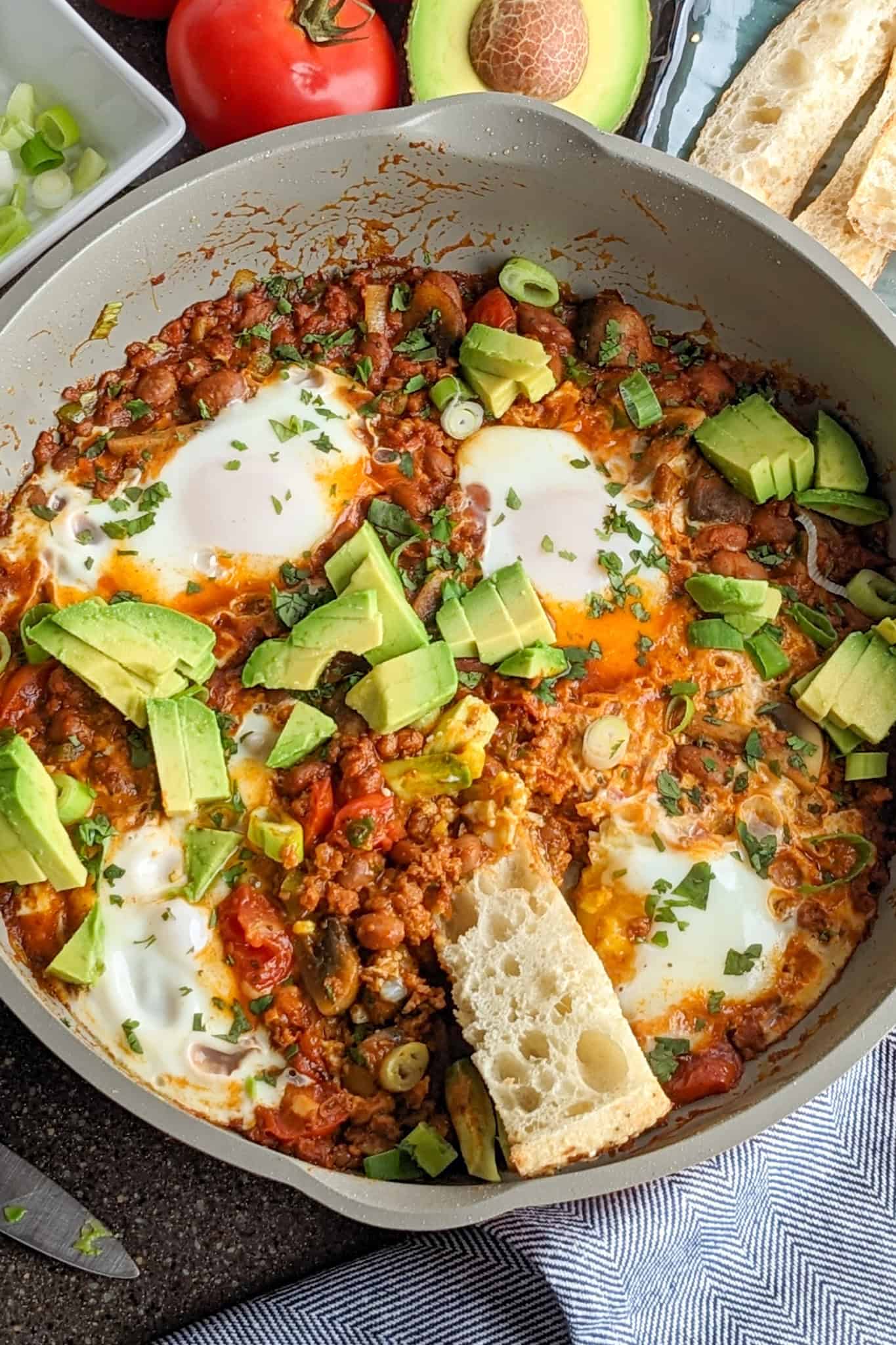 Colorful chorizo beans and poached eggs skillet topped with avocado and fresh herbs.